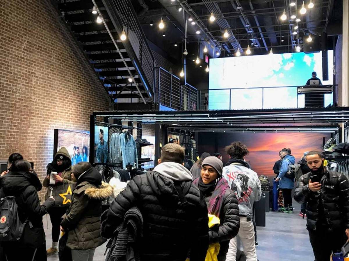 Shoppers browse clothing displays inside a modern retail store with digital screens and industrial-style lighting.