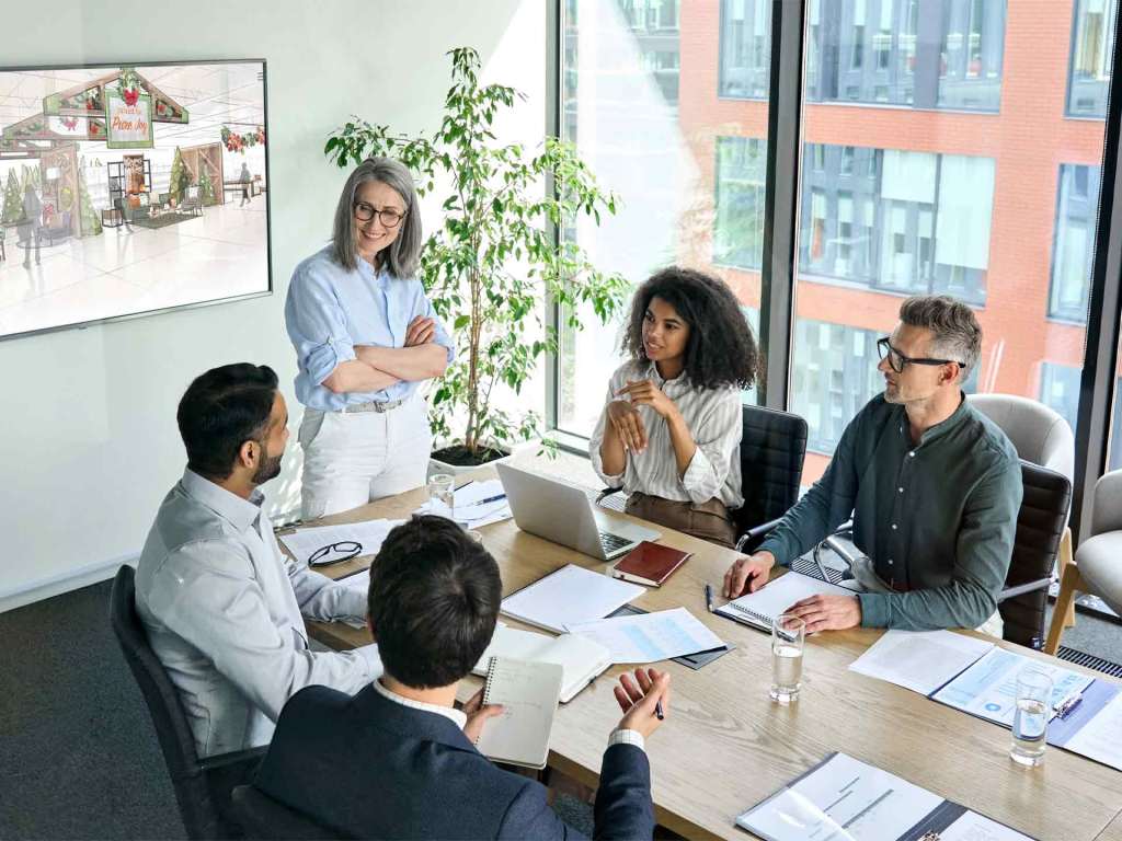 Diverse creative team in a modern conference room discussing a retail store concept on a large display screen.