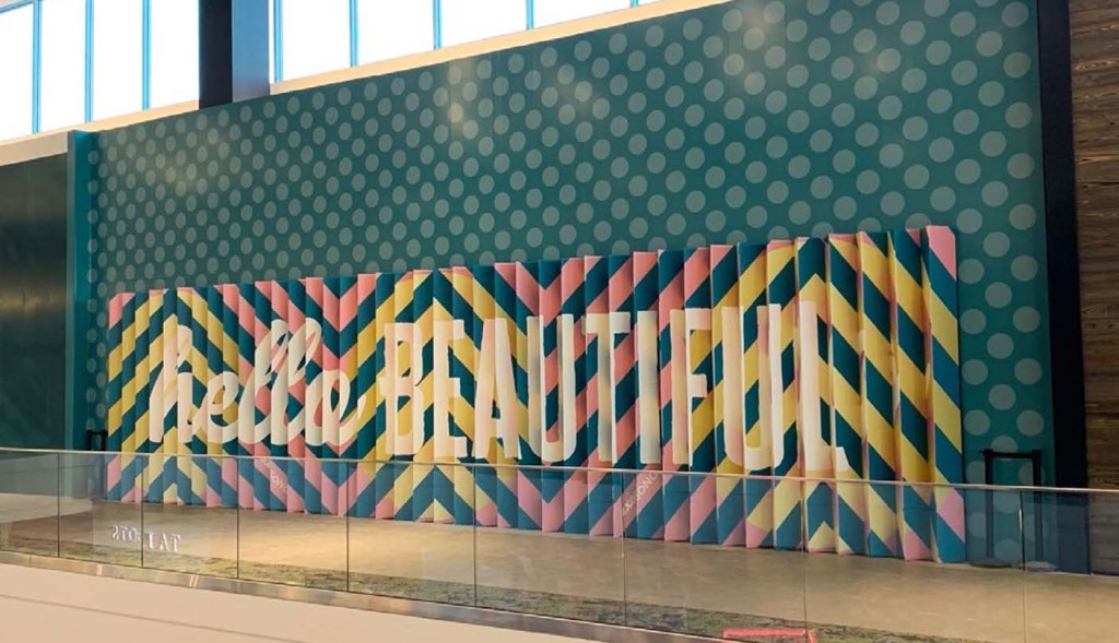 Colorful "hello BEAUTIFUL" accent wall mural with pleated chevron pattern in a mall.
